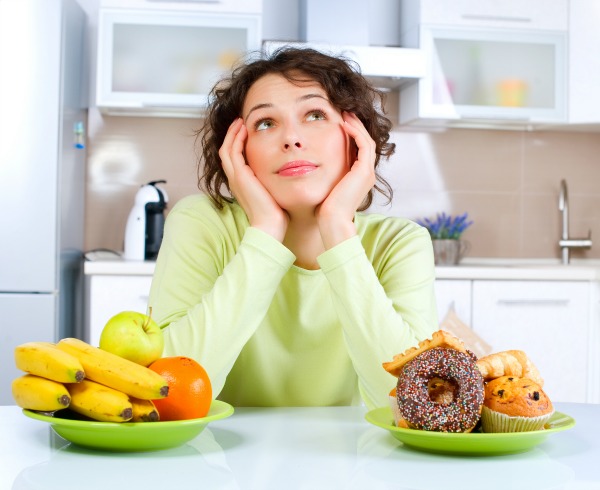 Young woman choosing between Fruits and Sweets